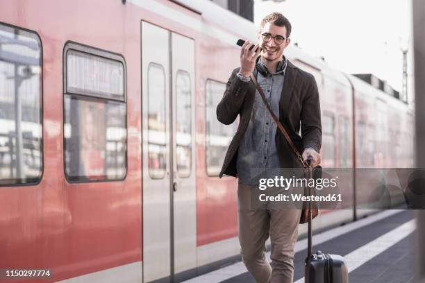 happy young man with cell phone walking on station platform along commuter train - train station stock-fotos und bilder