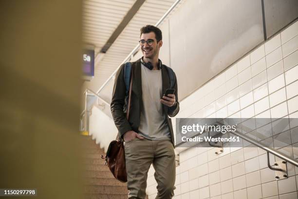 smiling young man with cell phone walking down stairs at the station - underpass stock pictures, royalty-free photos & images