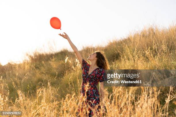 happy young woman standing in summer meadow, letting go of a red balloon - loslassen aktivitäten und sport stock-fotos und bilder