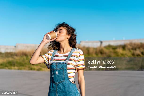 young woman drinking coffee from a disposable cup - women drinking coffee stock-fotos und bilder