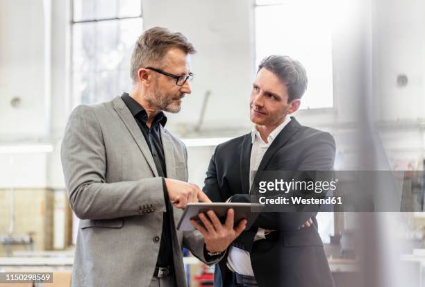 two businessmen with tablet discussing in a factory - business suits discussion stock-fotos und bilder