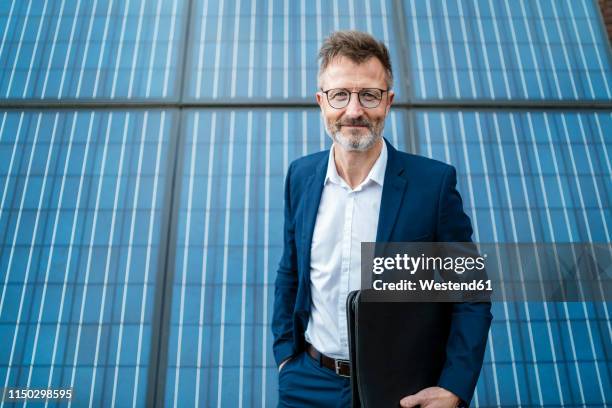 portrait of smiling businessman holding folder standing in front of solar panels - unternehmerische sozialverantwortung stock-fotos und bilder