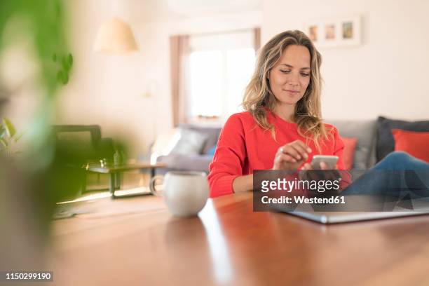 woman using cell phone on dining table at home - smartphone zuhause stock-fotos und bilder