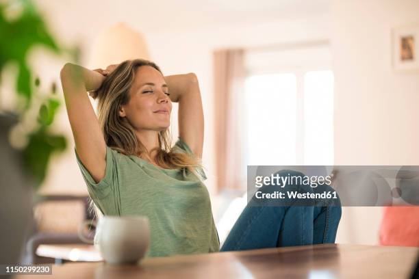 woman sitting at dining table at home relaxing - tevreden stockfoto's en -beelden