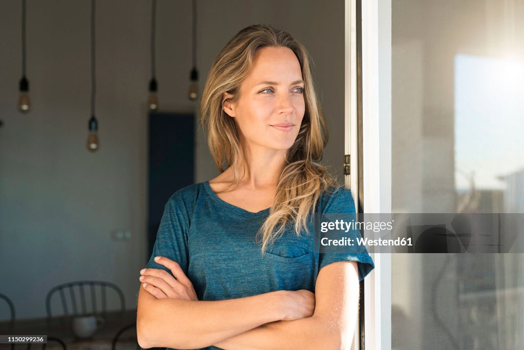 Woman leaning at open window at home looking sideways