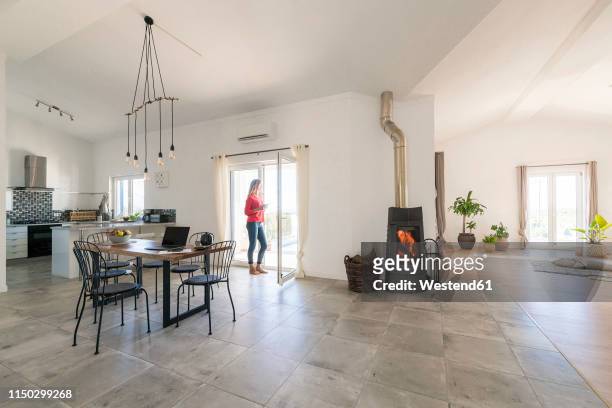 woman standing in door frame of modern living room with fireplace - distant fire stock pictures, royalty-free photos & images