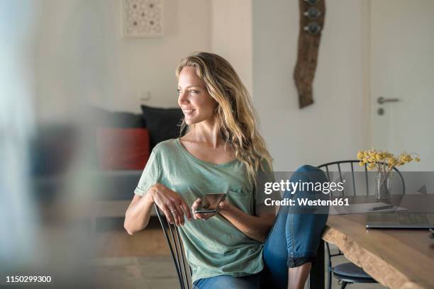 smiling woman with cell phone and laptop on dining table at home - woman looking away stock pictures, royalty-free photos & images