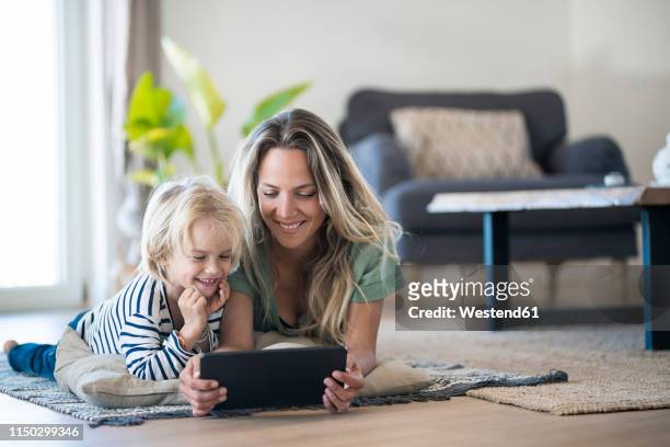 smiling mother and son lying on the floor at home using tablet - parents watching kids bildbanksfoton och bilder