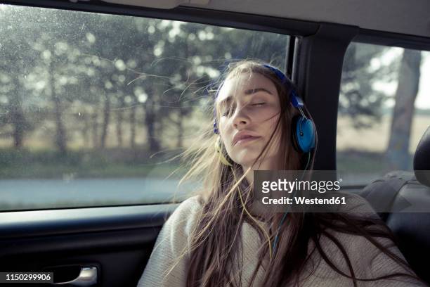 young woman with windswept hair in a car wearing headphones - sensory perception stockfoto's en -beelden