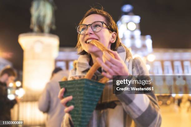 spain, madrid, young woman in the city at night eating typical churros with chocolate - churro stockfoto's en -beelden