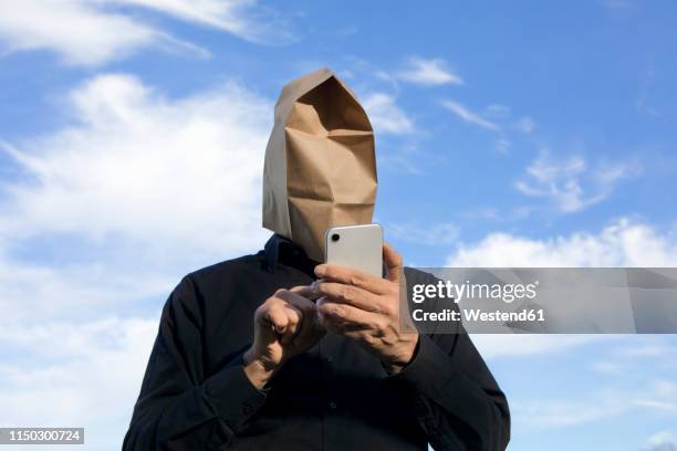 man with paper bag above his head using cell phone - crazy man computer stock-fotos und bilder