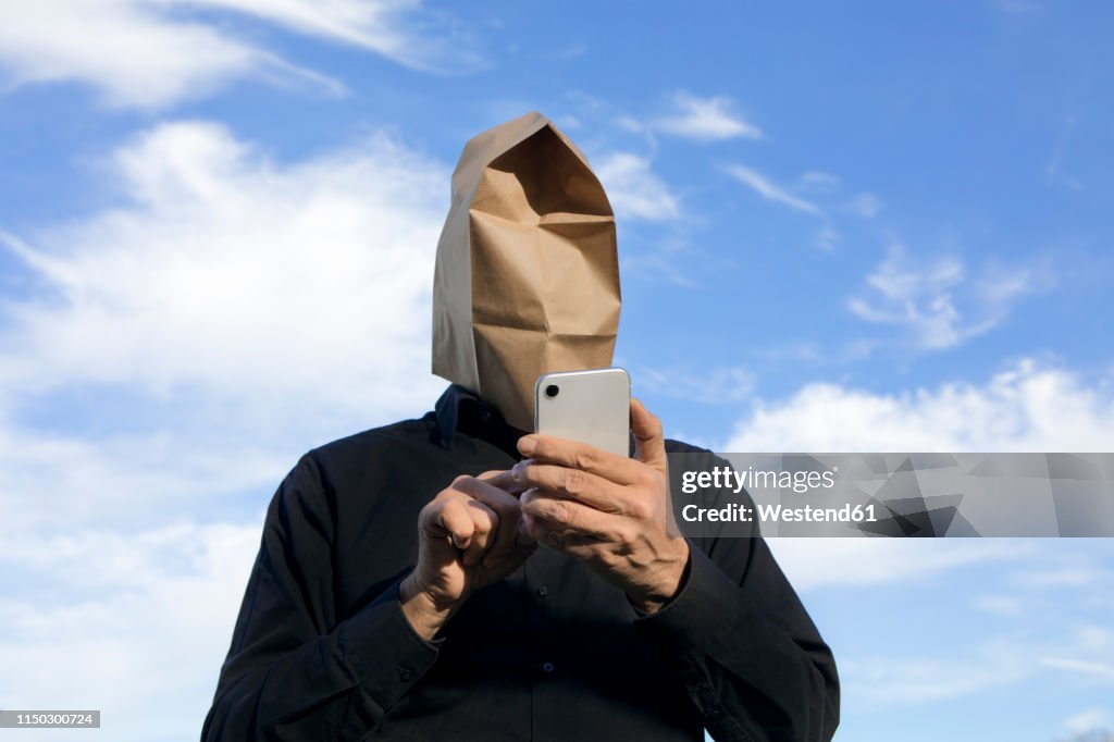 Man with paper bag above his head using cell phone