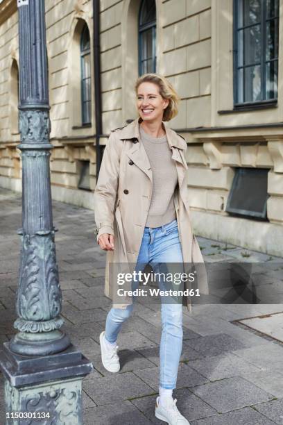 happy woman walking on pavement in the city - weißer mantel stock-fotos und bilder
