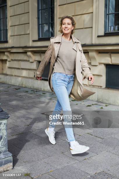 happy woman walking on pavement in the city - coat stock-fotos und bilder