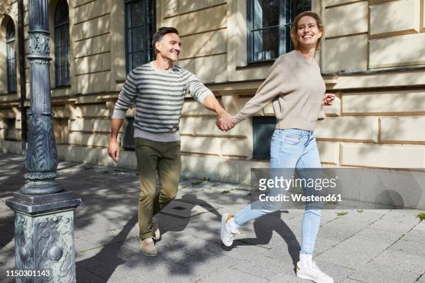 happy couple running on pavement in the city - happy people running stockfoto's en -beelden