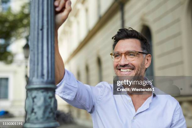 portrait of happy businessman leaning against lamp post in the city - casual businessman glasses white shirt stock pictures, royalty-free photos & images