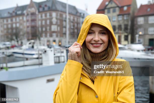 denmark, copenhagen, portrait of happy woman at city harbour in rainy weather - frau mit gelben regenmantel stock-fotos und bilder