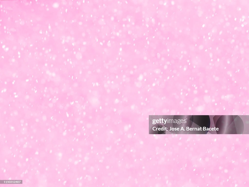 Background of snowflakes of snow that fall down from the sky on a light pink bottom.