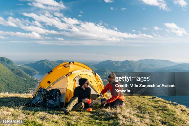 couple camping on mountain top, prepare food and beverages next to tent - camp site foto e immagini stock