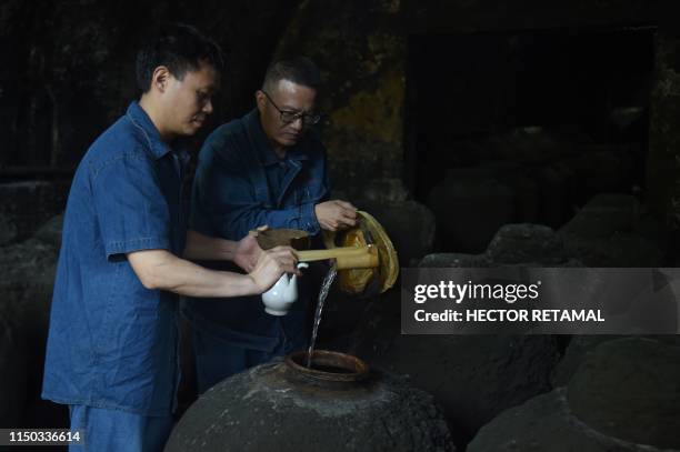 In this photo taken on April 22 workers inspect a container filled with baijiu liquor in a cave located in the hills of Luzhou, southwestern China's...