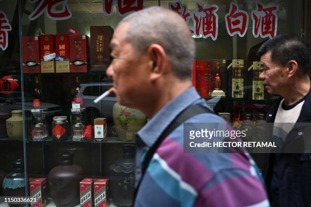 In this photo taken on April 24 people walk past a shop selling selling bottles of baijiu liquor in Luzhou, southwestern China's Sichuan province. -...