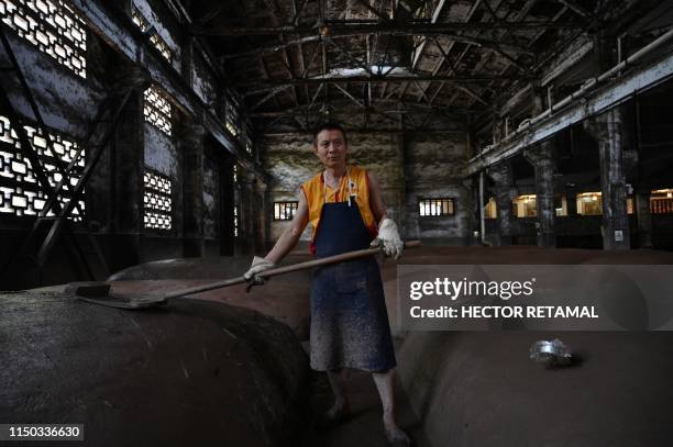 In this photo taken on April 22 a worker poses beside mounds where grain is fermented at the Luzhou Laojiao distillery where baijiu is produced in...