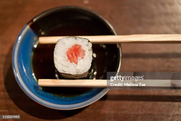 tuna maki sushi with chopsticks in soy sauce - shoyu stockfoto's en -beelden