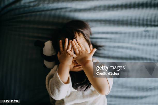 portrait of cute little asian toddler girl covering her face playing peekaboo while lying on bed with panda soft toy lying next to her - baby sleeping stockfoto's en -beelden