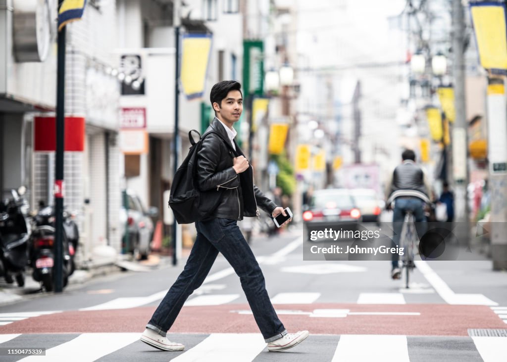 Cool japansk man i sin 20s korsning gata på zebra korsning