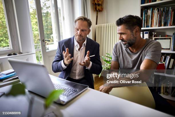 businessman and casual man sitting at desk with laptop - tipping hat stock-fotos und bilder