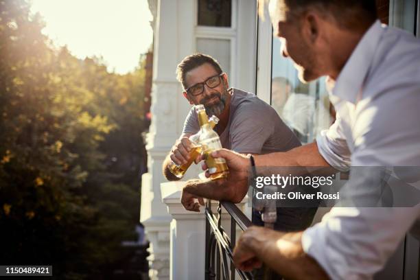 two mature men having a beer on balcony - friends drinking foto e immagini stock
