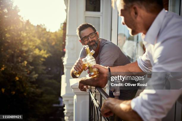 two mature men having a beer on balcony - man beer stock pictures, royalty-free photos & images