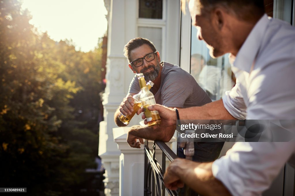 Two mature men having a beer on balcony