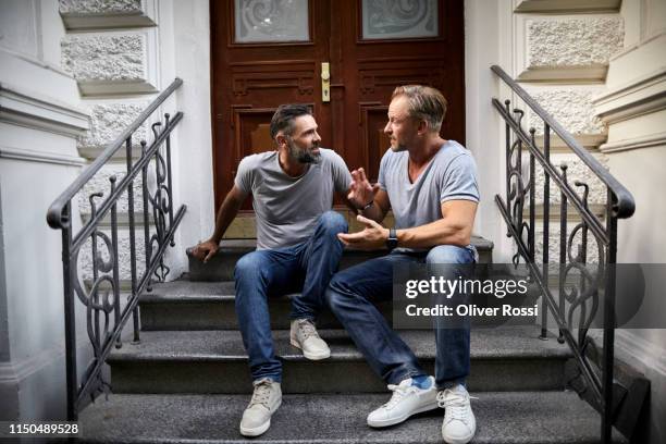 two mature male friends sitting on front stoop talking - stoop stock pictures, royalty-free photos & images