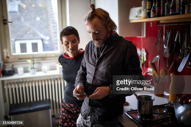 Mature couple using cell phone in kitchen at home