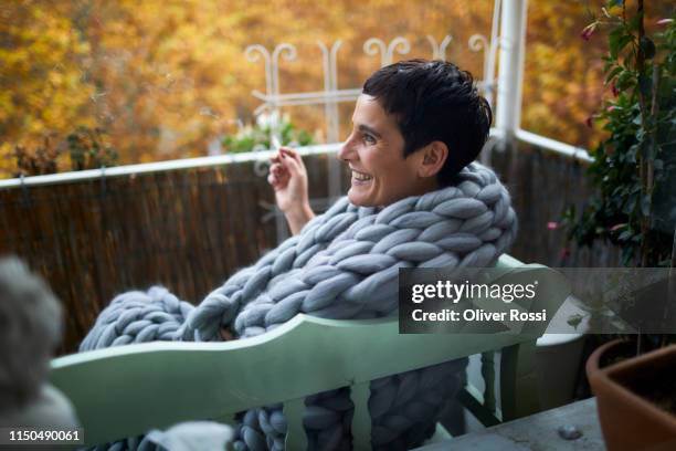 mature woman wrapped in a blanket smoking a cigarette on balcony - woman smoking cigarette stock-fotos und bilder