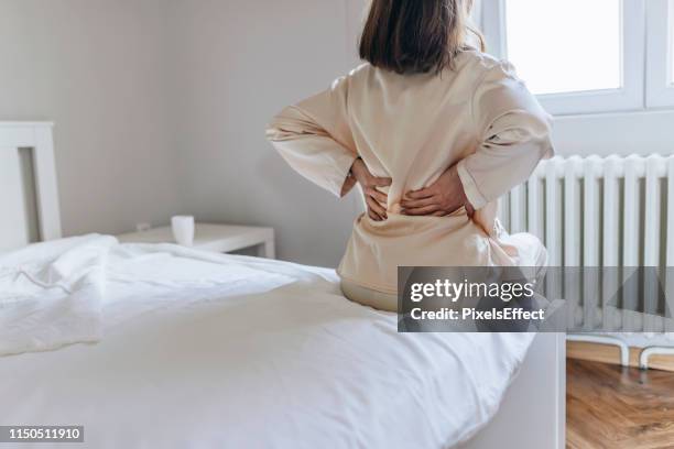 woman feels back pain massaging aching muscles - sciatic nerve stock pictures, royalty-free photos & images
