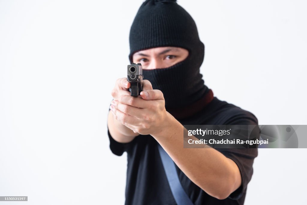 Burglar or terrorist in black mask shooting with gun isolated on white background