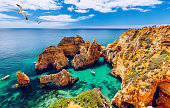 Panoramic view, Ponta da Piedade with seagulls flying over rocks near Lagos in Algarve, Portugal. Cliff rocks, seagulls and tourist boat on sea at Ponta da Piedade, Algarve region, Portugal.