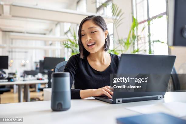 mujer profesional usando asistente virtual en el escritorio - altavoz inteligente fotografías e imágenes de stock