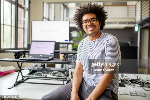 portrait of smiling young professional sitting at desk - man with curly hair stock pictures, royalty-free photos & images