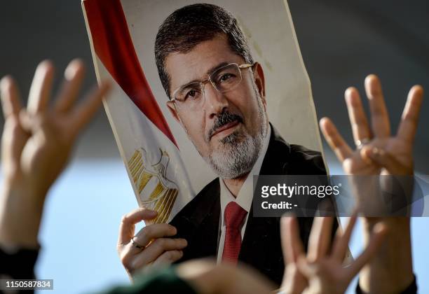People flashes Rabia sign , next to a poster of former Egyptian President Mohamed Morsi as people attend symbolic funeral ceremony on June 18,2019 at...