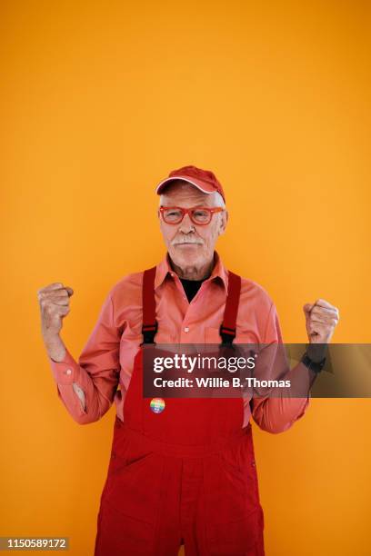 portrait of senior gay man in red overalls - senior studio portrait stock-fotos und bilder