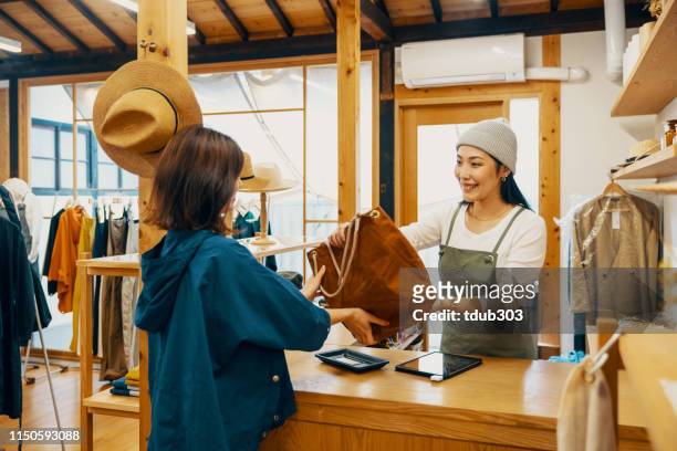 young woman buying a bag using mobile payment at a clothjing store - small business saturday stock pictures, royalty-free photos & images
