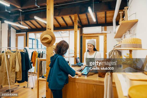 female small business owner accepting mobile payment via digital tablet in a clothing store - sunday stock pictures, royalty-free photos & images