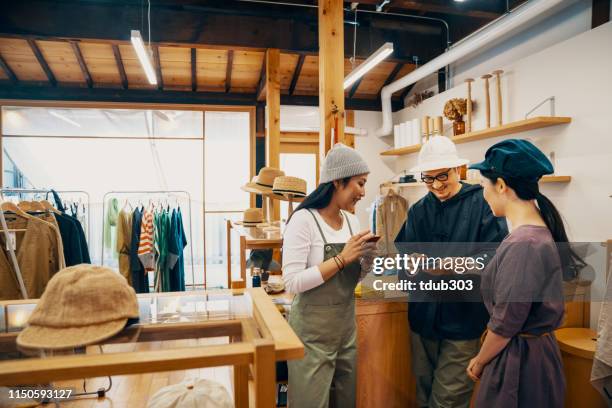 three millenial aged people looking at their smart phones in a clothing store - small business saturday stock pictures, royalty-free photos & images