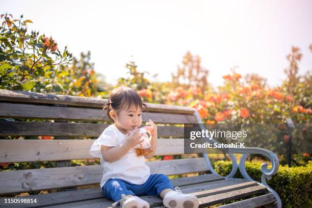 baby girl drinking apple juice in public park - apple juice stock pictures, royalty-free photos & images