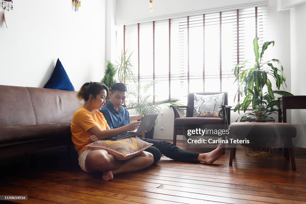 Young Chinese couple sitting on the floor at home with a laptop