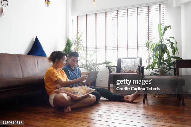 young chinese couple sitting on the floor at home with a laptop - asian young couple stock pictures, royalty-free photos & images