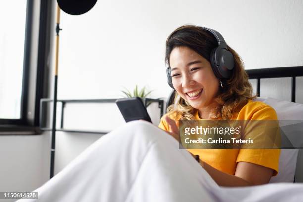 woman reading from her smart phone in bed, smiling - chinese music imagens e fotografias de stock